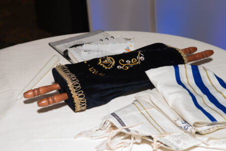 A sacred Jewish Torah scroll containing the Pentateuch, written by a scribe on kosher animal parchment and displayed open for reading during a service." An open Jewish Torah scroll made of parchment, showcasing traditional hand-written Hebrew calligraphy in black ink, attached to two decorative wooden rollers.